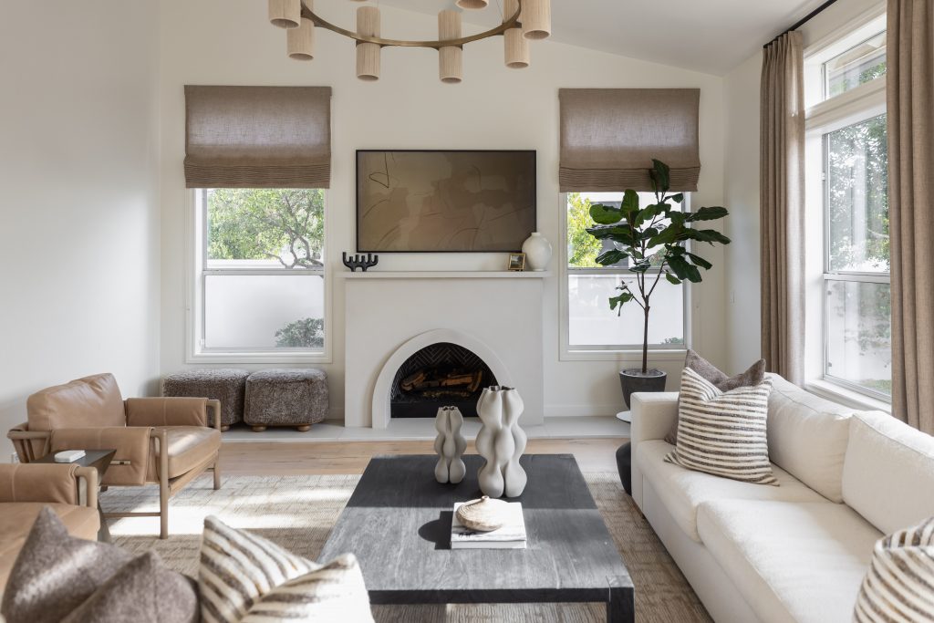 Modern living room with a white sofa, brown chairs, black coffee table, fireplace, wall-mounted TV, and large windows—Living with Lolo.