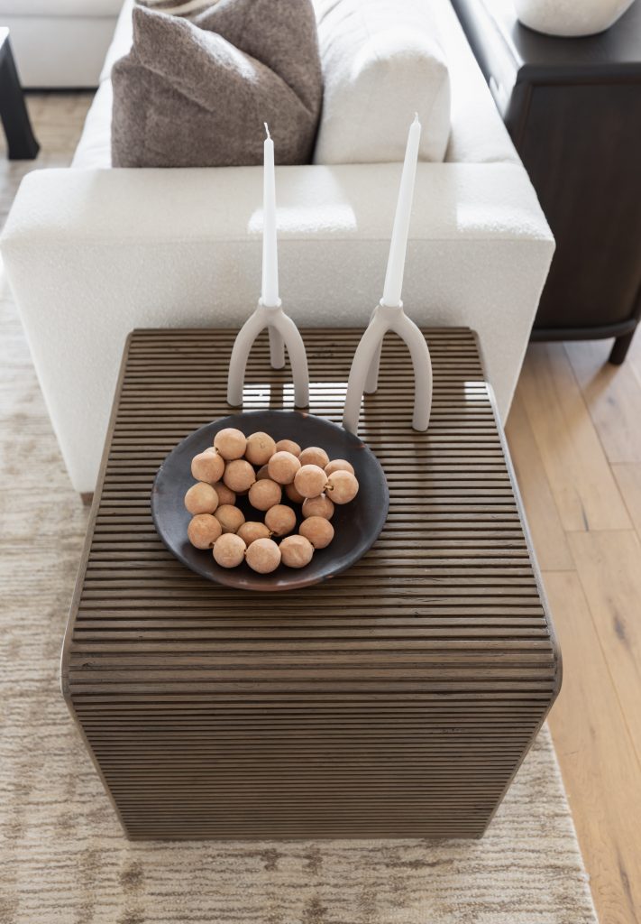 A wooden side table with a black plate of walnuts and two white candlesticks stands beside a white couch. — Living with Lolo.