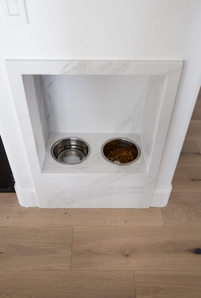 Built-in feeding station with two bowls set into a white marble alcove, positioned against a white wall on wooden flooring—Living with Lolo.
