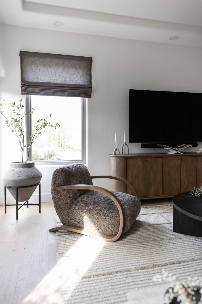 A modern living room with a textured armchair, wooden cabinet, flat-screen TV, potted plant, and window with brown shade. — Living with Lolo.