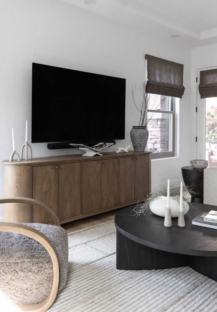 A modern living room features a wall-mounted TV above a wooden cabinet, a dark coffee table, and neutral-toned furniture and rugs. — Living with Lolo.