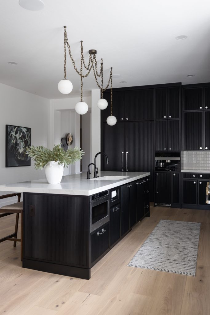 Modern kitchen featuring black cabinets, white countertops, an island with built-in appliances, globe pendant lights, and light wood flooring—Living with Lolo.