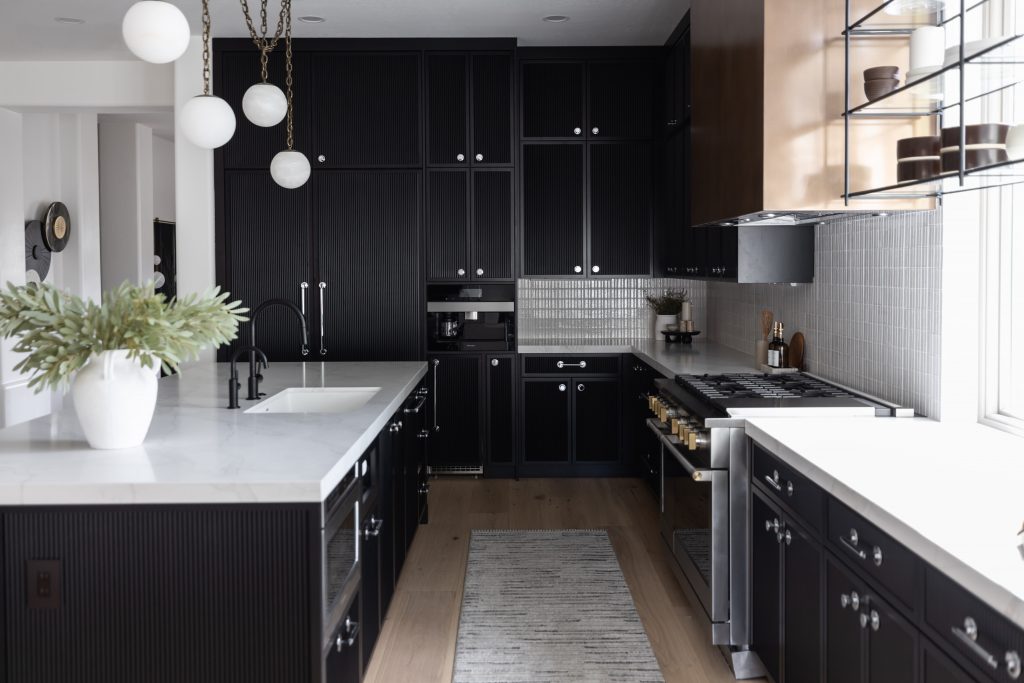 Modern kitchen with black cabinets, white countertops, stainless steel appliances, globe lights, and a potted plant on the island— Living with Lolo.