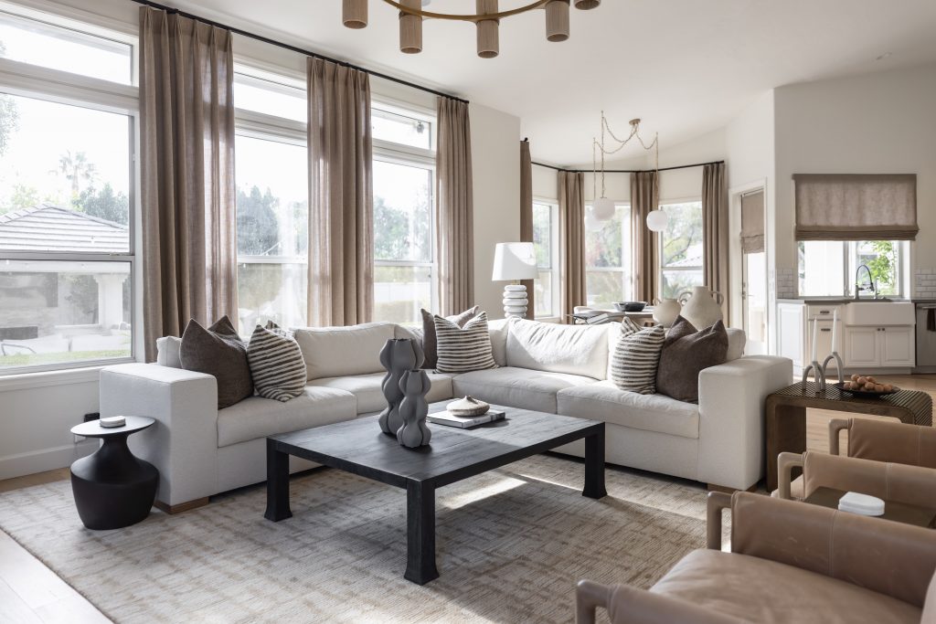 Modern living room with a beige sectional sofa, black coffee table, neutral decor, and large windows with sheer curtains—Living with Lolo.