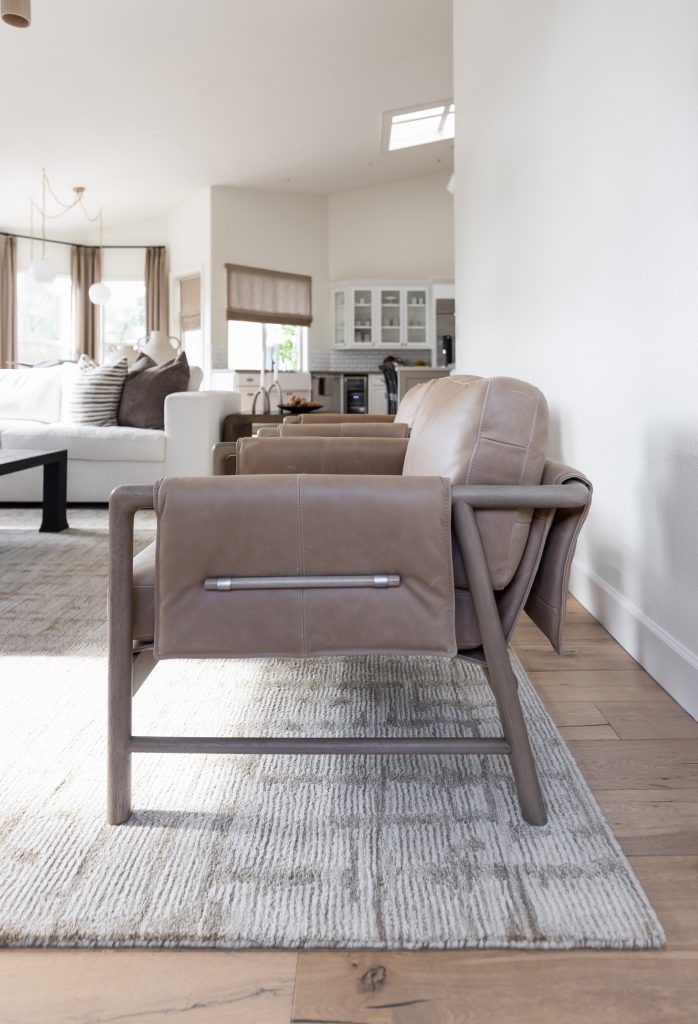 A tan leather armchair with a metal frame is on a patterned rug in an open living room with a sofa and kitchen visible—Living with Lolo.