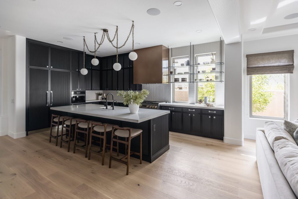 Modern kitchen featuring dark cabinets, a large island with seating, wood floors, and expansive windows—Living with Lolo.