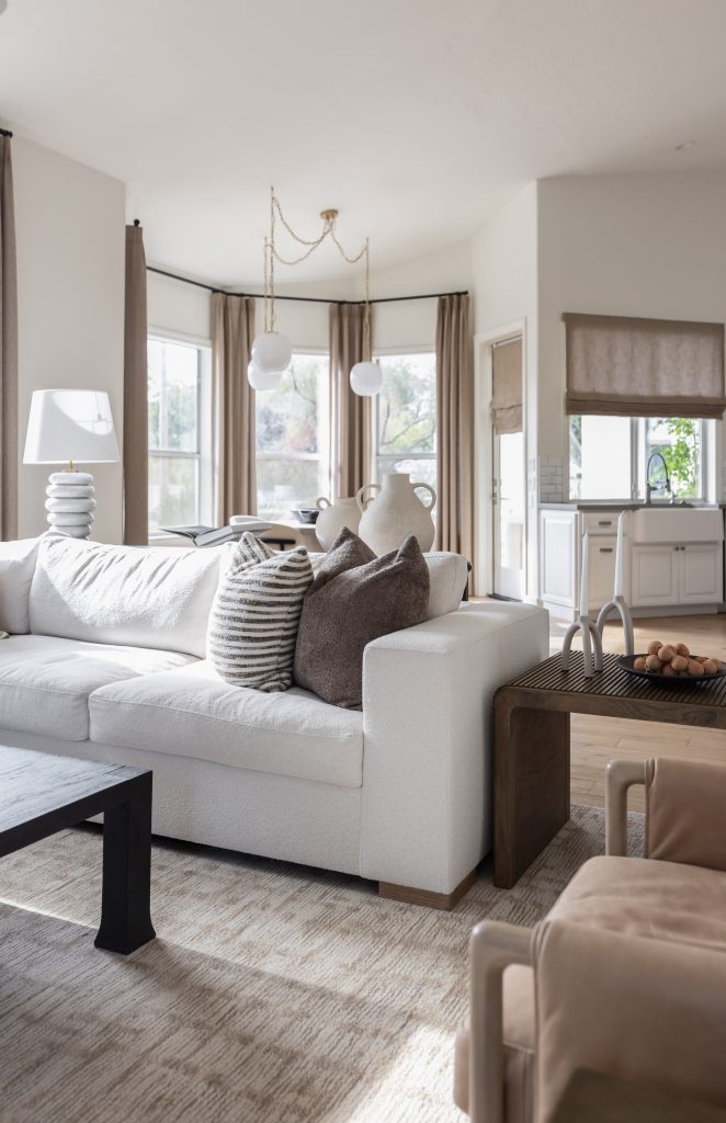White sofa with assorted pillows, a coffee table, large windows, and an updated kitchen area in the background — Living with Lolo.