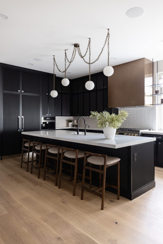 Modern kitchen with black cabinets, a large island topped with a white countertop, four wooden stools, and a potted plant centerpiece—Living with Lolo.