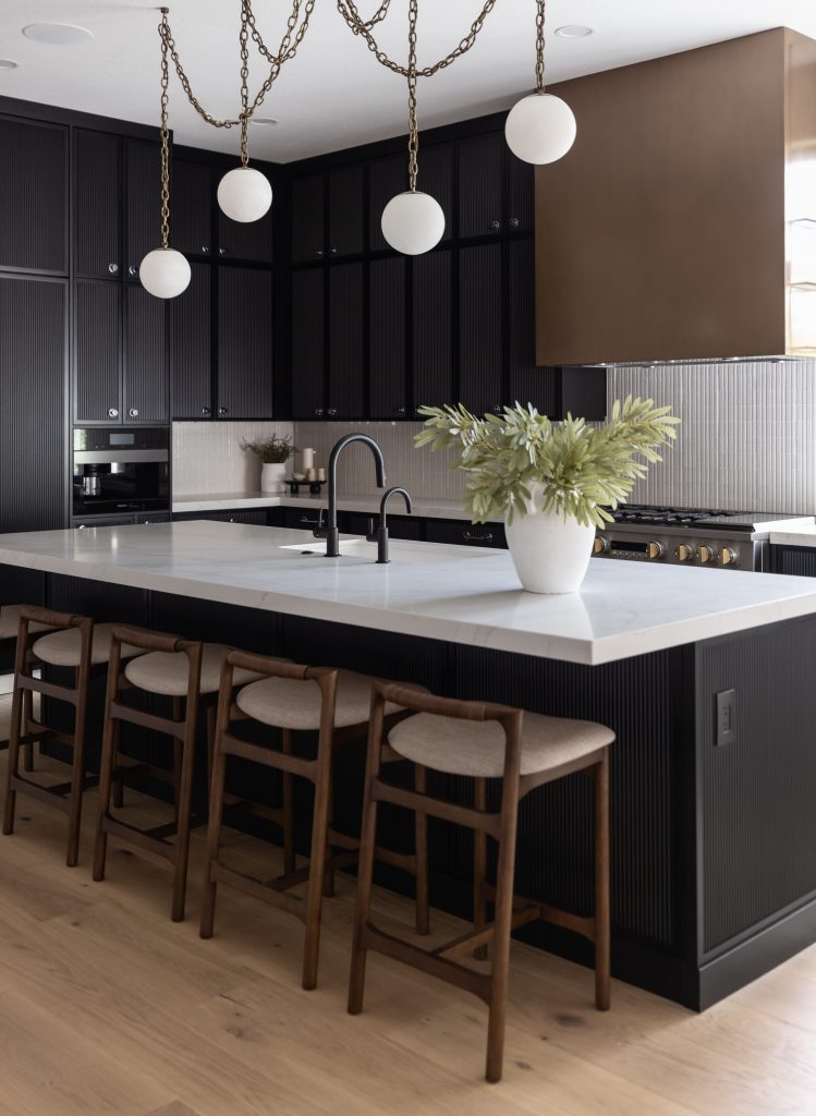 Modern kitchen with black cabinets, white countertops, a large island with four wooden stools, globe pendant lights, and a potted plant centerpiece— Living with Lolo.
