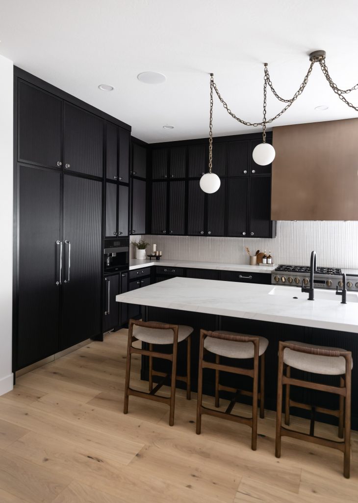 Modern kitchen with dark cabinets, a white marble island, three wooden barstools, light wood floors, and two globe pendant lights—Living with Lolo.