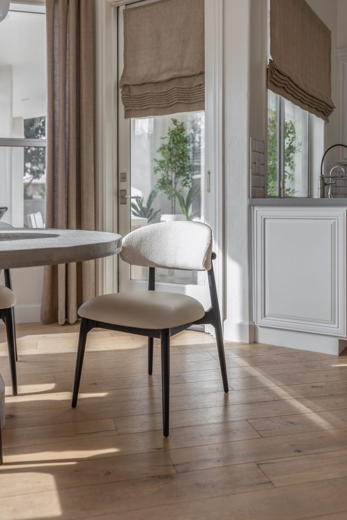 A modern dining chair and round table are placed in a bright room with wooden floors, beige curtains, and Roman shades — Living with Lolo.
