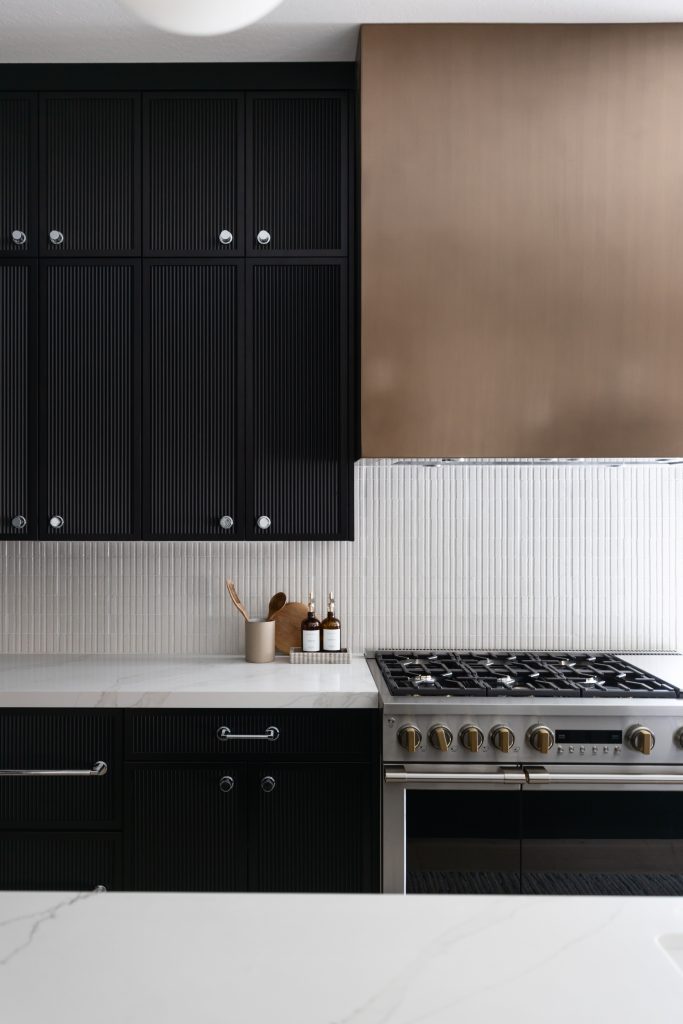 Modern kitchen featuring black cabinets, a white marble countertop, vertical white tile backsplash, and a stainless steel gas stove—Living with Lolo.