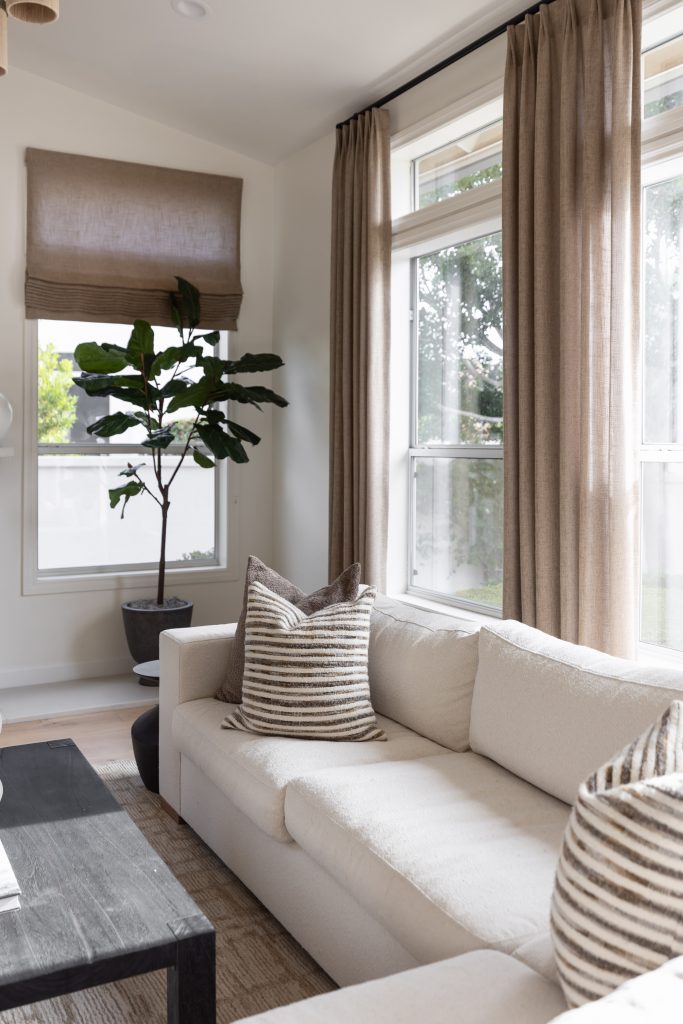 A cream sofa with striped pillows, a black coffee table, beige curtains, and large windows are shown. — Living with Lolo.