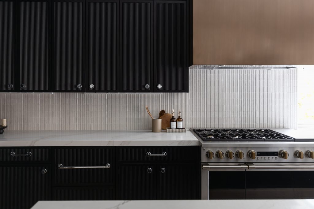 Modern kitchen featuring dark cabinets, a white tile backsplash, marble countertop, and a stainless steel stove—Living with Lolo.