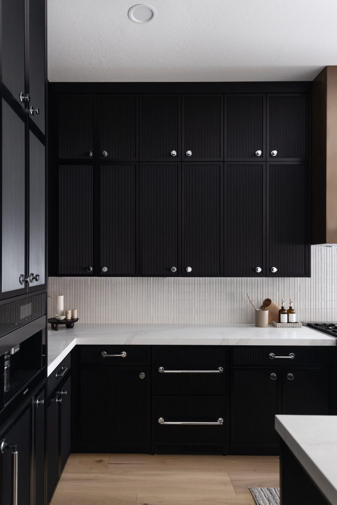Kitchen with matte black cabinets, white countertops, light wood floors, and a few candles and utensils on the counter. — Living with Lolo.