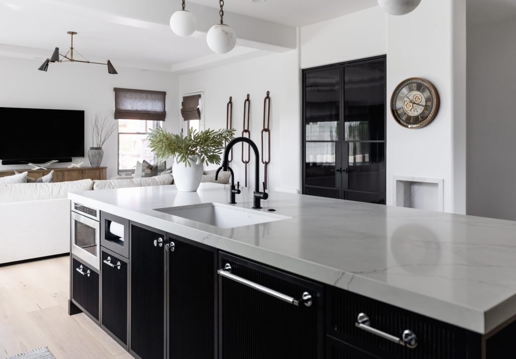 Modern kitchen featuring a white marble island, black cabinetry, built-in appliances, and a black faucet; living area in background—Living with Lolo.
