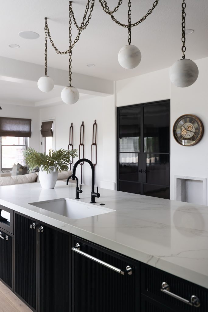 A kitchen with a white marble island, black cabinets, matte black sink fixtures, globe pendant lights, and a glass cabinet.— Living with Lolo.