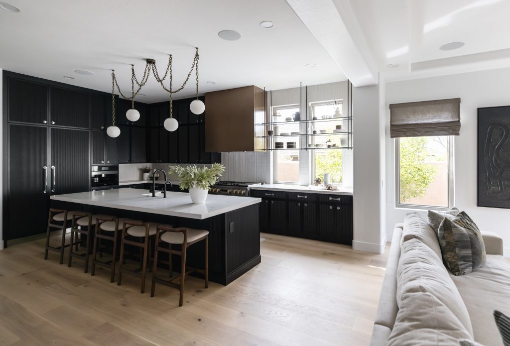 Black kitchen cabinets, a white island with four stools, pendant lights, light wood floors, and large windows. Part of a sofa is in view — Living with Lolo.