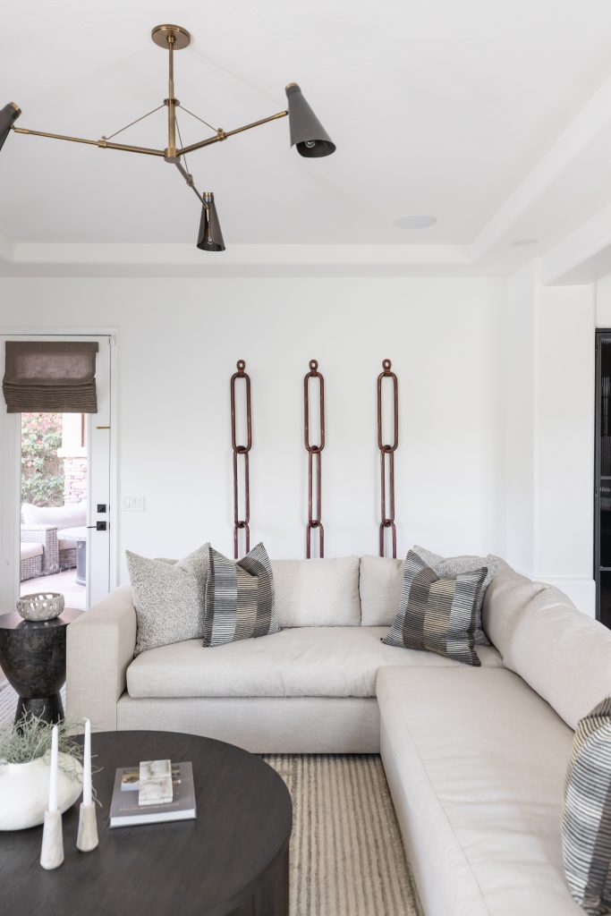 Modern living room with a light-colored sectional sofa, patterned throw pillows, a round dark coffee table, and three vertical wall art pieces— Living with Lolo.