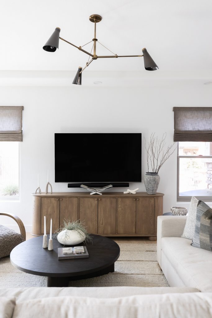 A living room with a light sofa, round black coffee table, wooden media console, large TV, and minimalist decor. — Living with Lolo.