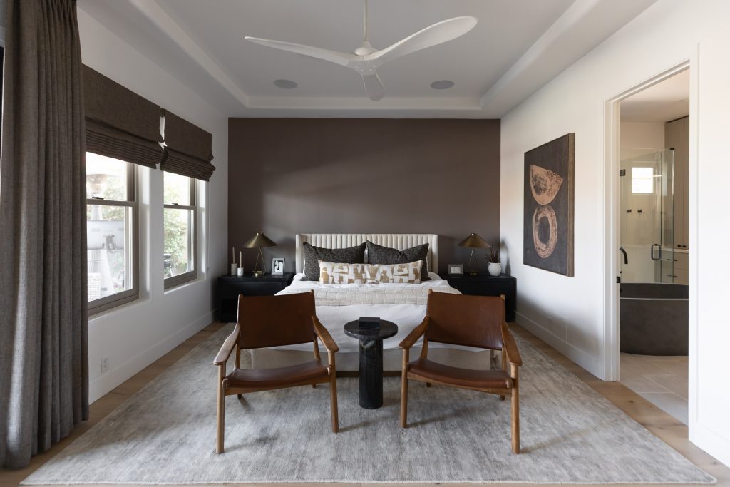 Modern bedroom featuring a double bed, two brown leather chairs, a black table, large windows, and an attached bathroom—Living with Lolo.