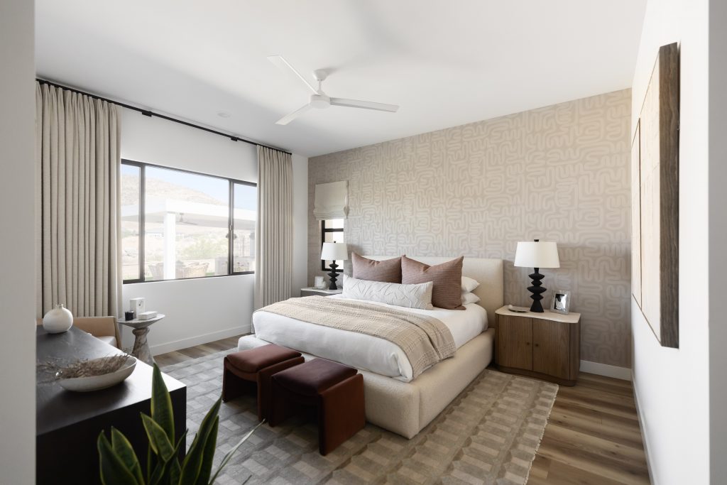 A modern bedroom with a large bed, two nightstands, neutral bedding, brown ottomans, curtained window, and a patterned accent wall — Living with Lolo.
