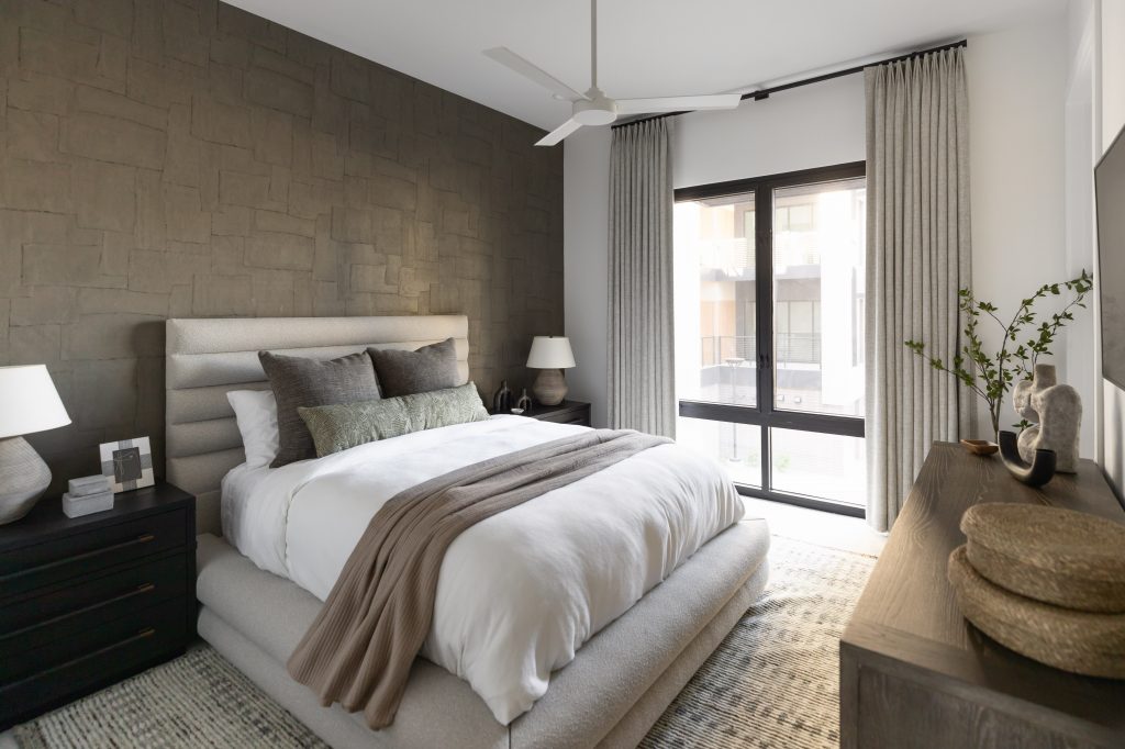 Modern bedroom featuring a large bed with neutral bedding, bedside tables with lamps, a dresser, and a window with curtains—Living with Lolo.