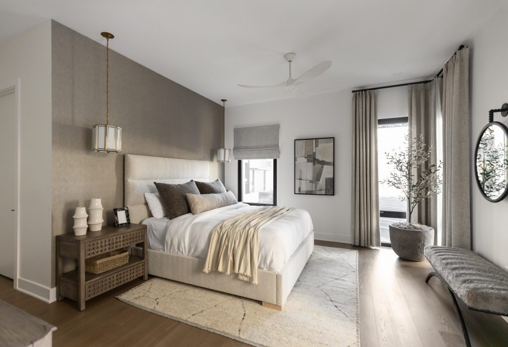 Modern bedroom featuring a large bed with neutral bedding, pendant lights, side table, bench, artwork, and a potted plant near curtained windows — Living with Lolo.