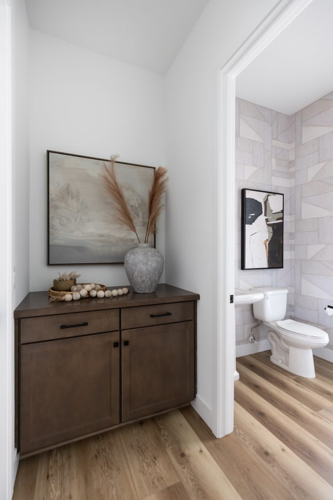 A hallway cabinet with a vase of dried grasses, wooden beads, and framed art sits beside a bathroom with abstract wall art. — Living with Lolo.