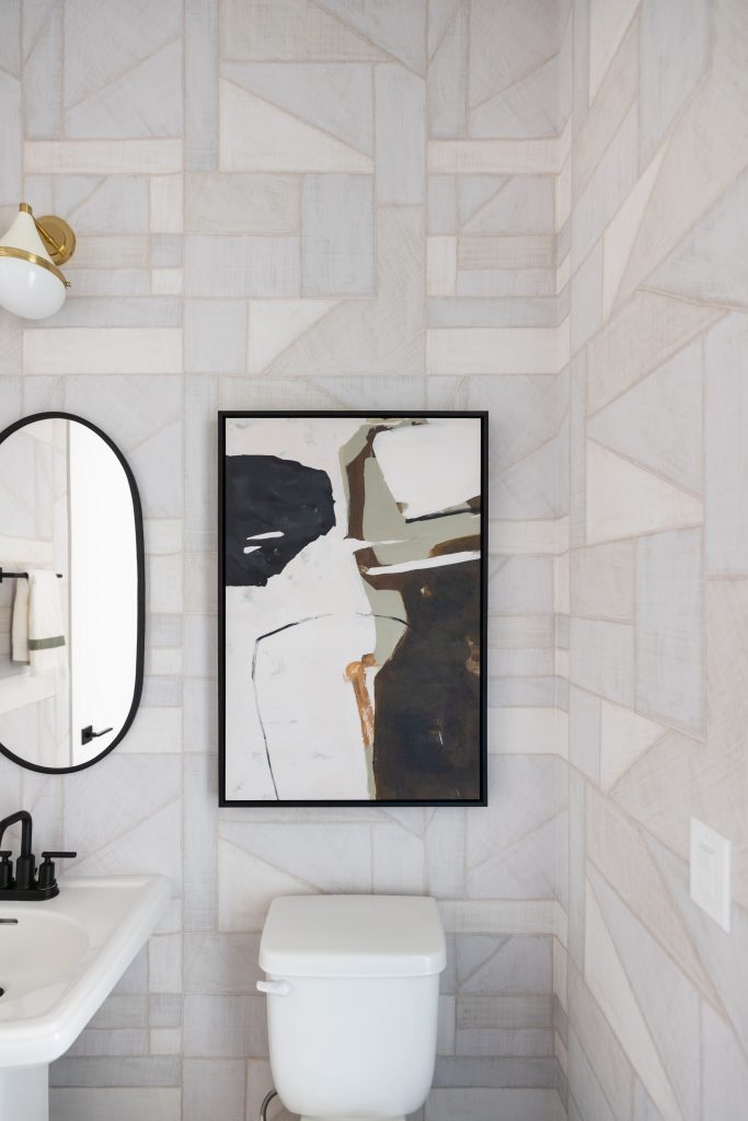 A bathroom with geometric wallpaper, a white toilet, abstract art above it, and a white sink with a black faucet. — Living with Lolo.