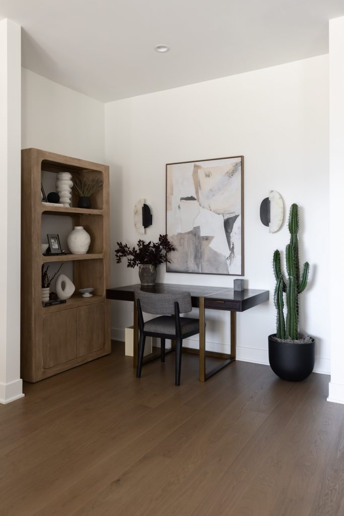 A wooden desk, black chair, abstract art, wall sconces, a tall potted cactus, and a bookshelf with decor are shown — Living with Lolo.