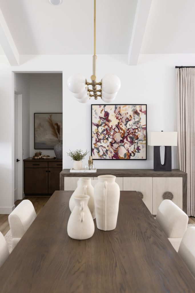 Dining room featuring a wooden table, cream chairs, three white vases, abstract wall art, a lamp, and a sideboard. — Living with Lolo.