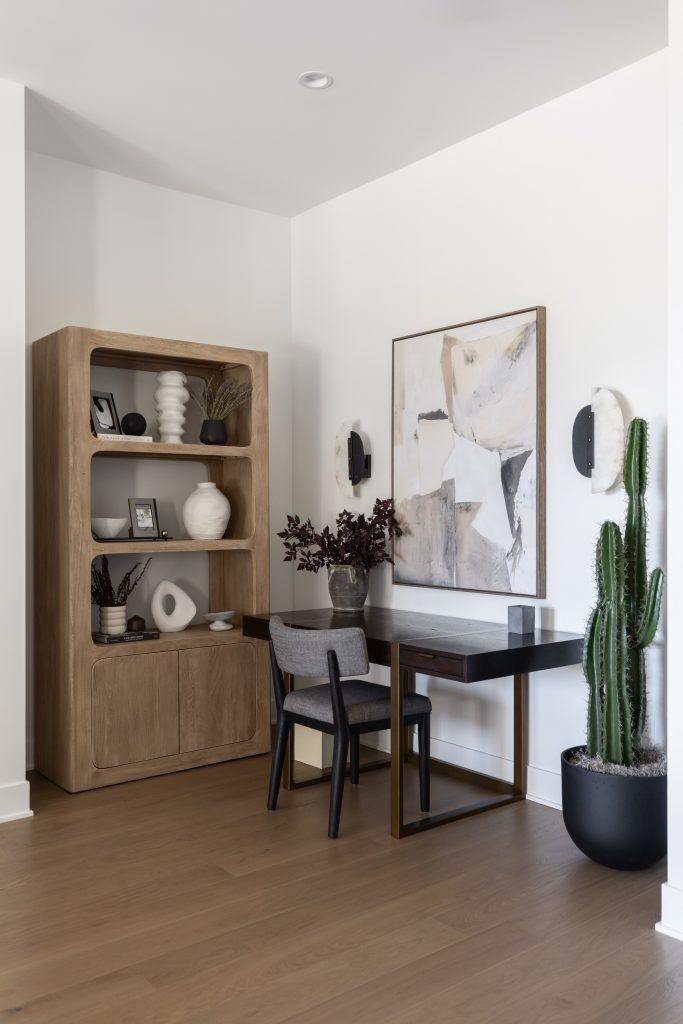 A wooden bookshelf, desk with chair, abstract wall art, two sconces, and a tall potted cactus in a minimalistic room. — Living with Lolo.