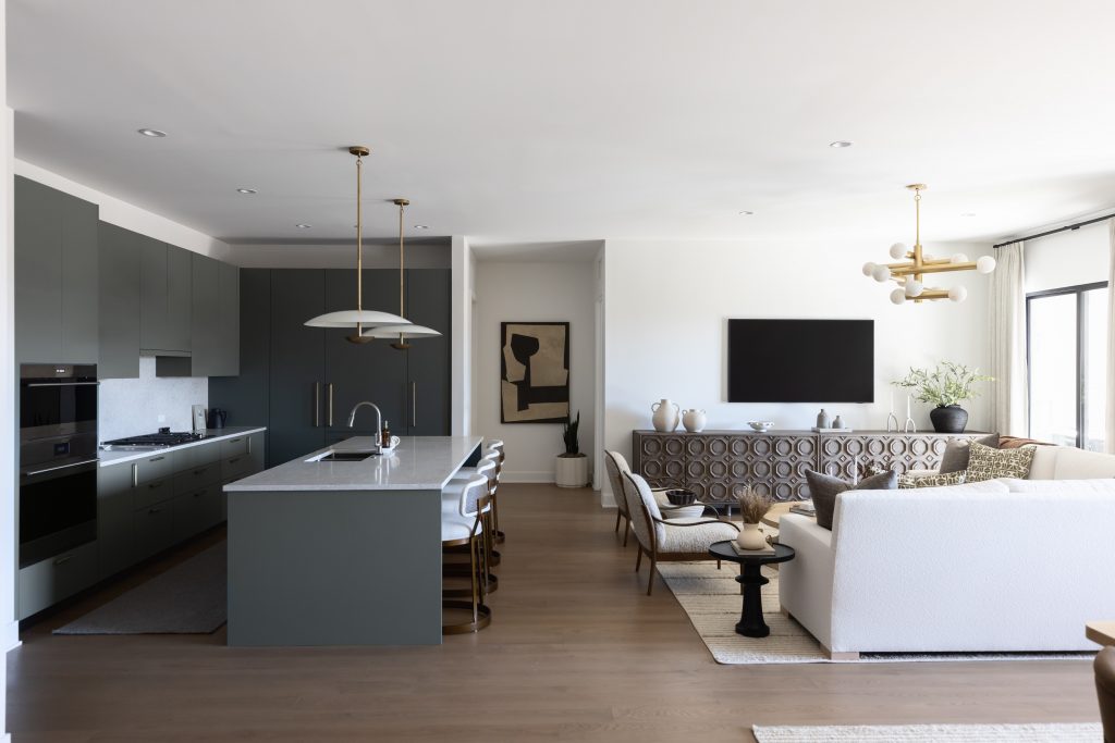 Open-plan kitchen and living room featuring green cabinetry, marble island, pendant lights, a patterned sofa, and wall art—Living with Lolo.