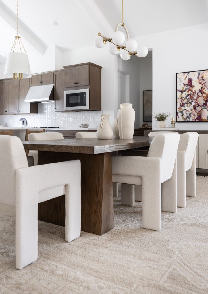 Modern dining room featuring a dark wooden table, cream upholstered chairs, ceramic vases, pendant lights, and an open kitchen—Living with Lolo.
