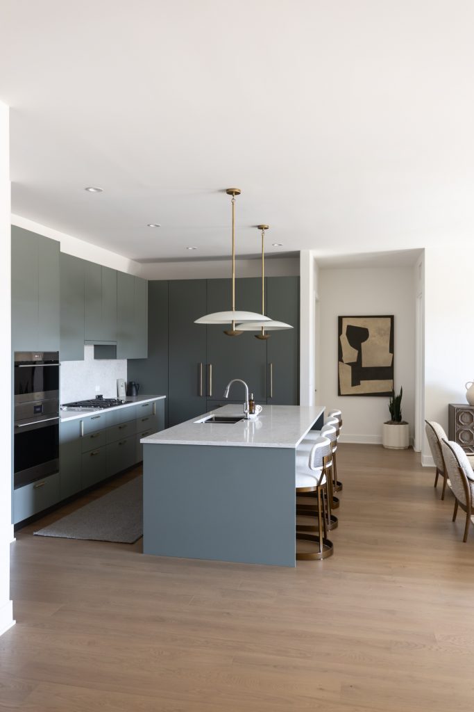 Modern kitchen with gray cabinets, a marble island, four bar stools, built-in appliances, pendant lights, and abstract wall art—Living with Lolo.