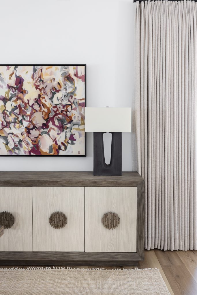 A modern sideboard with circular handles, a sculptural lamp, abstract wall art, and beige floor-length curtains. — Living with Lolo.