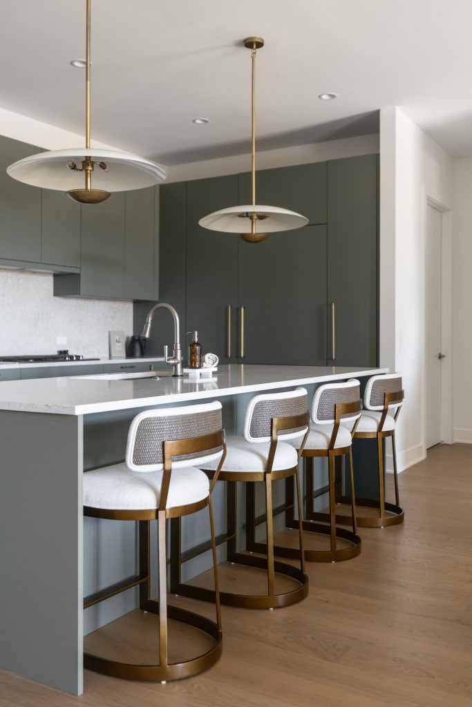 Modern kitchen with green cabinets, white countertops, brass fixtures, and four bar stools under two large pendant lights—Living with Lolo.