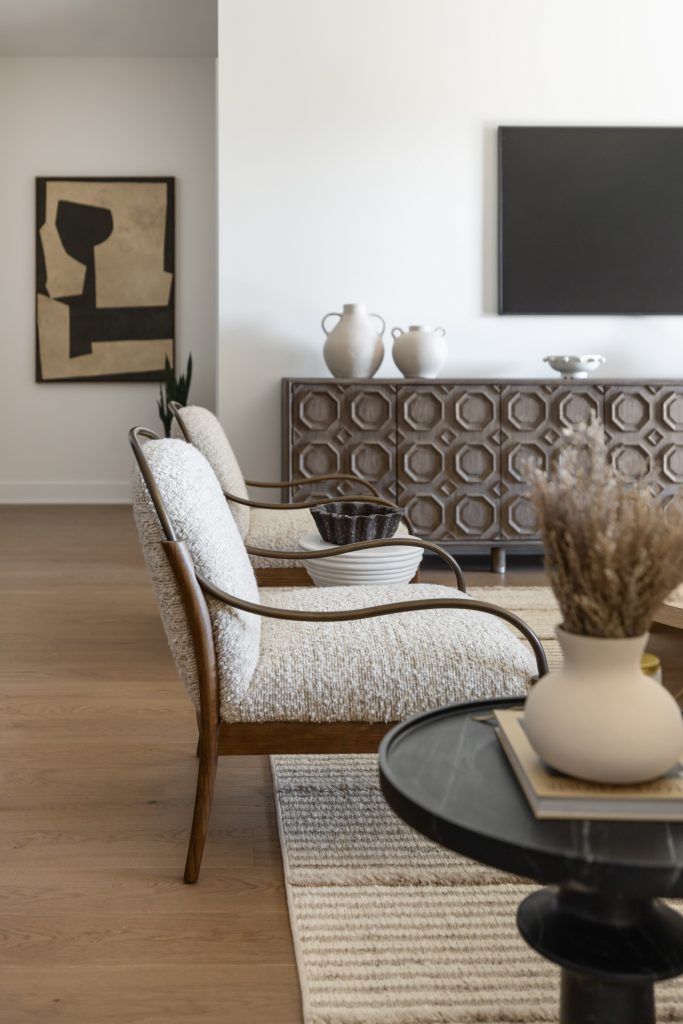 A living room with two cushioned chairs, a hexagonal-patterned sideboard, abstract wall art, TV, and vases on wood flooring — Living with Lolo.