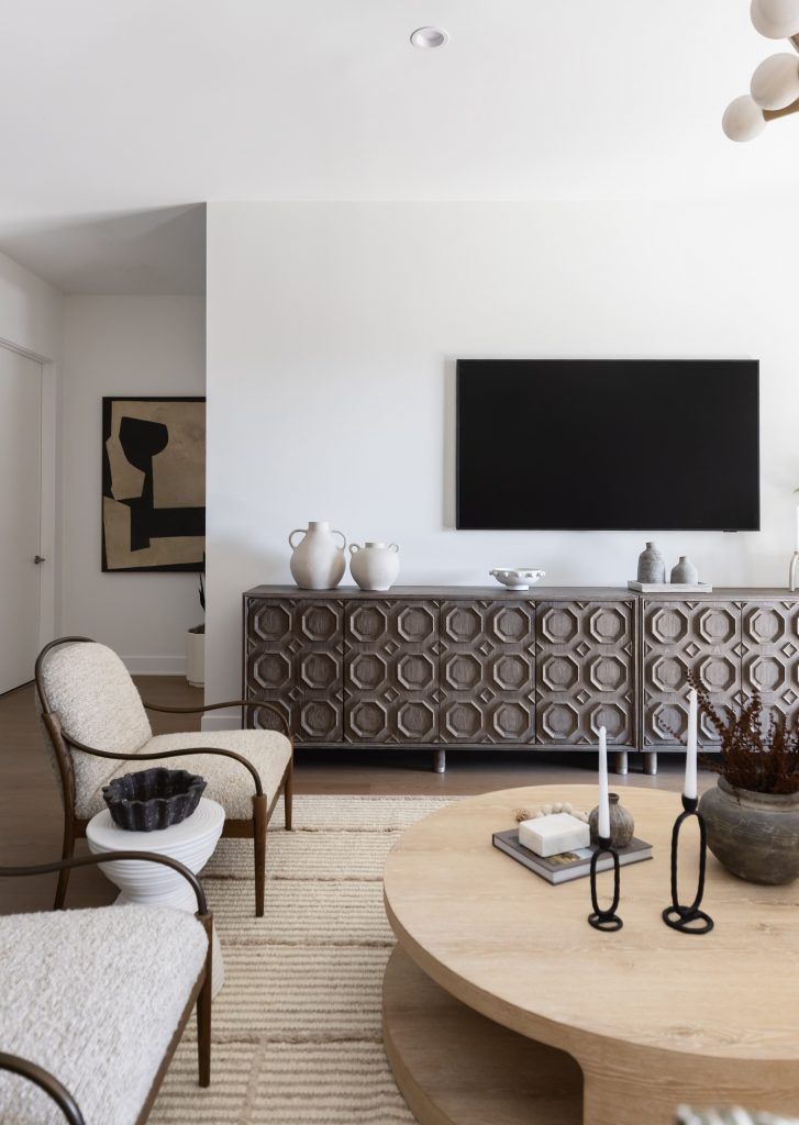 Modern living room with neutral colors, a patterned sideboard, wall-mounted TV, and round wooden coffee table—Living with Lolo.