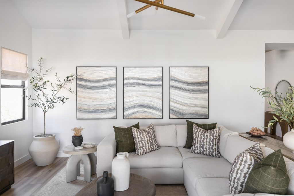 A modern living room displays a light gray sectional sofa, patterned pillows, abstract wave wall art, and neutral-toned accents—Living with Lolo.
