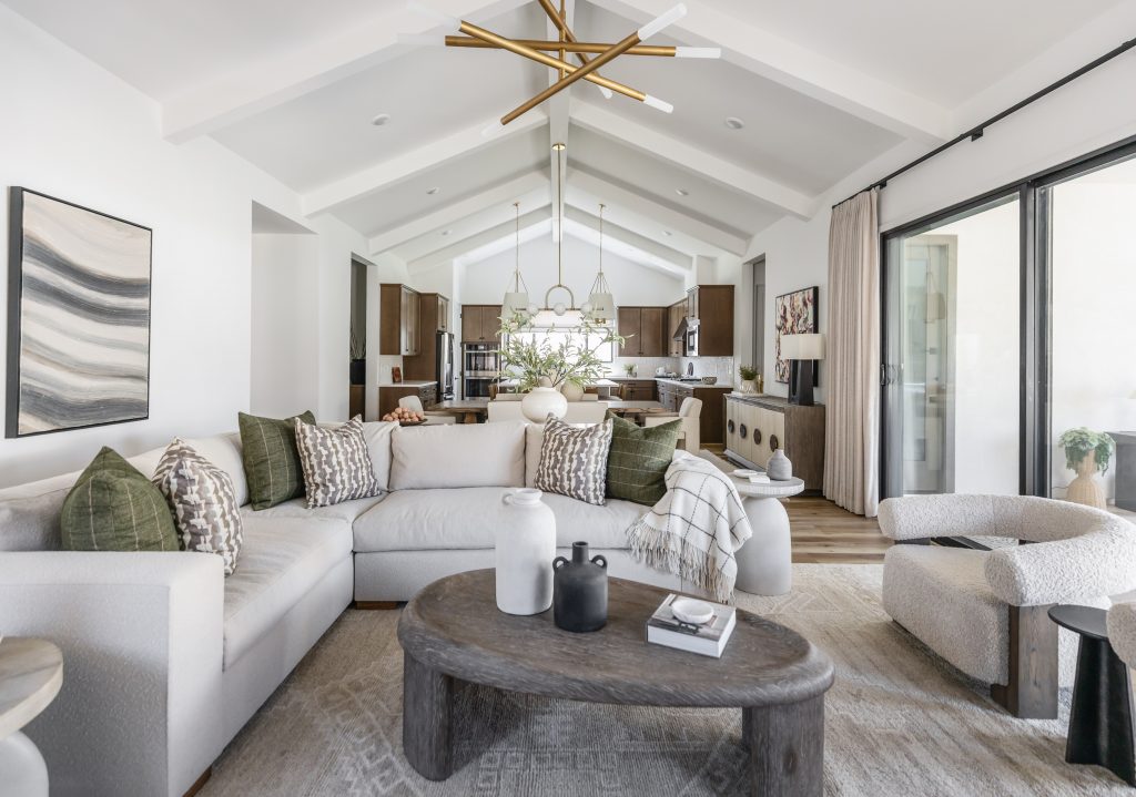 Modern living room with a white sectional sofa, wooden coffee table, neutral decor, and open kitchen with vaulted ceiling—Living with Lolo.