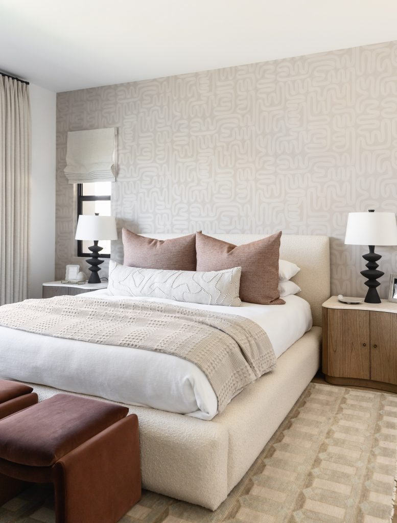 A modern bedroom with a beige upholstered bed, patterned accent wall, black bedside lamps, and neutral bedding.— Living with Lolo.