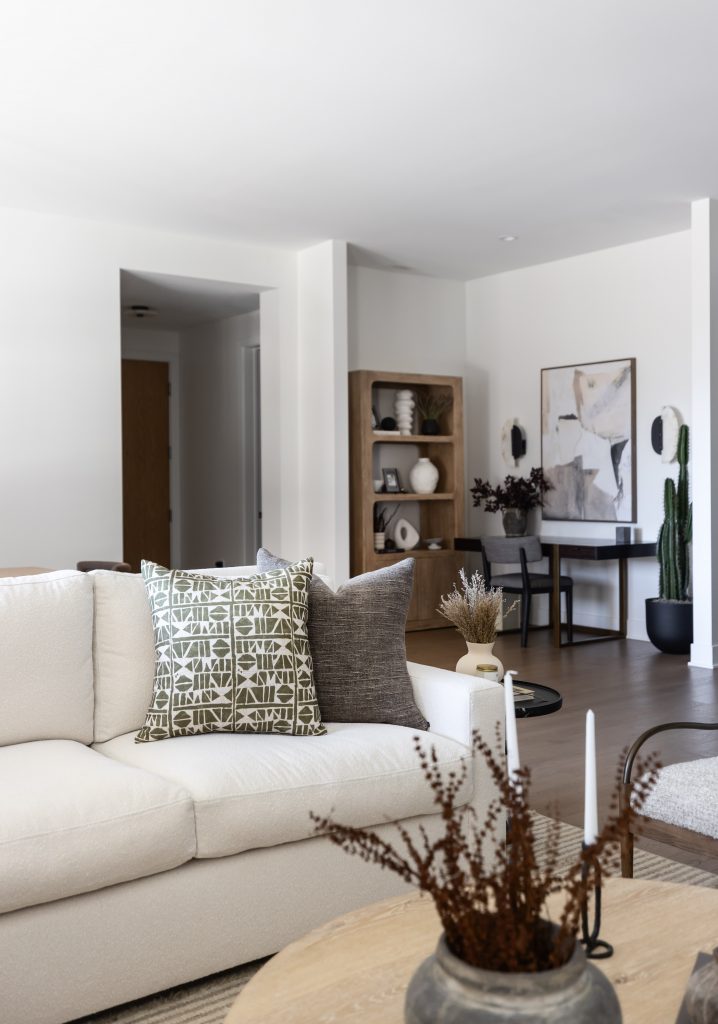 A modern living room with a white sofa, patterned and gray pillows, wooden coffee table, desk area with shelves, and abstract art. — Living with Lolo.