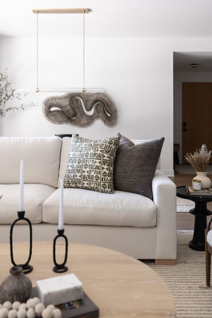 A white sofa with patterned and solid pillows, abstract wall art, two black candle holders, and a round wooden coffee table. — Living with Lolo.