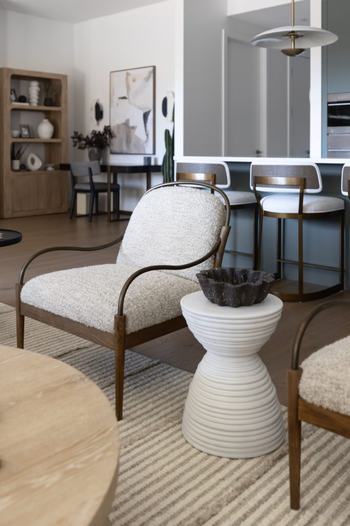 Modern living room featuring a textured armchair, white ribbed side table, striped rug, and bar stools at a kitchen counter—Living with Lolo.