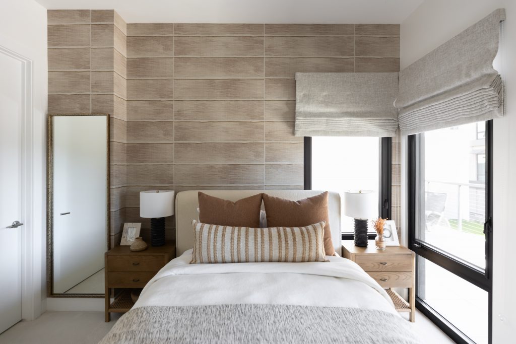 A modern bedroom with a beige bed, wooden nightstands, matching lamps, a tall mirror, tiled accent wall, and large windows.— Living with Lolo.