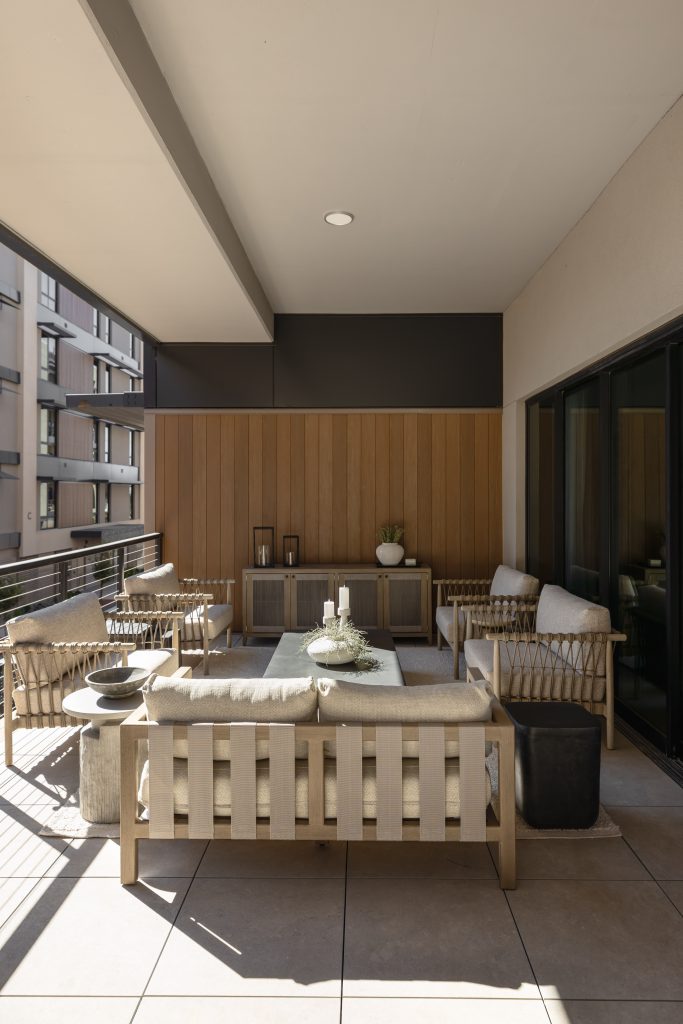 A modern outdoor patio with beige cushioned seating, a coffee table, potted plants, and wooden wall paneling—Living with Lolo.
