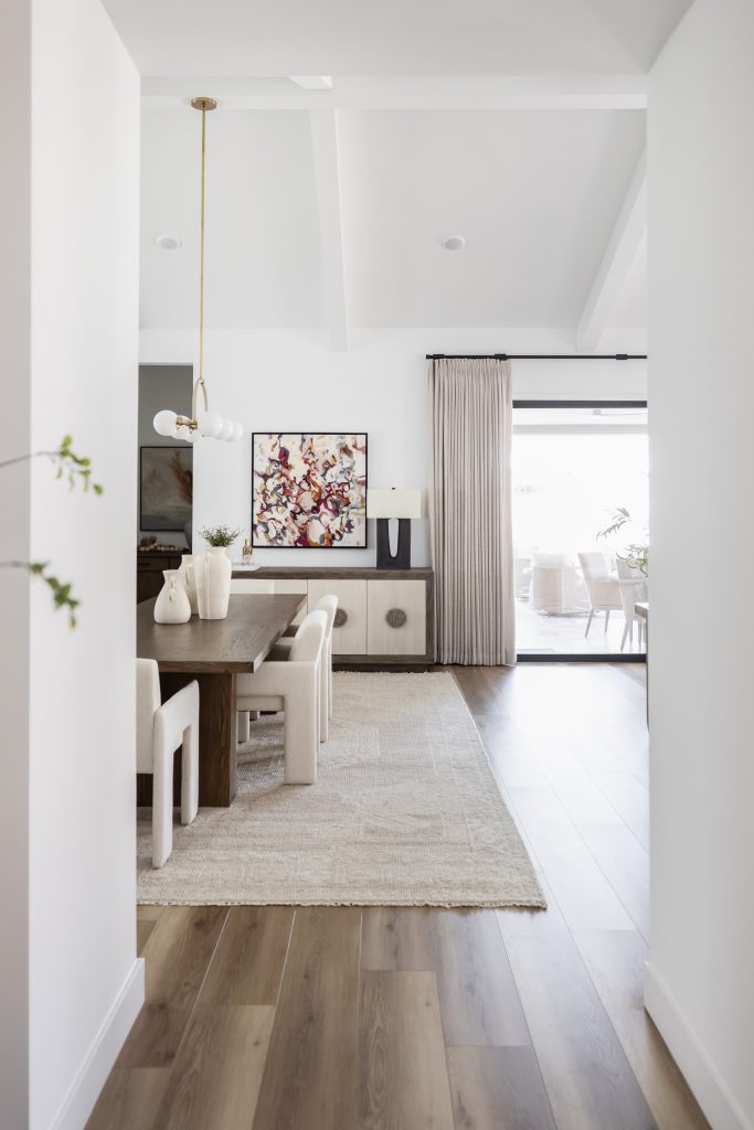 A modern dining room with a wooden table, cream chairs, light rug, abstract wall art, sideboard, and sliding glass doors. — Living with Lolo.