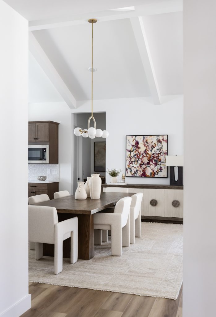 A dining room with a dark wood table, six upholstered chairs, chandelier, sideboard, abstract wall art, and light wood flooring — Living with Lolo.